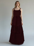 Ageless.ee deep burgundy tiered pleated maxi dress with embellished bodice, velvet waistband, and delicate straps. Model is wearing a formal evening gown.