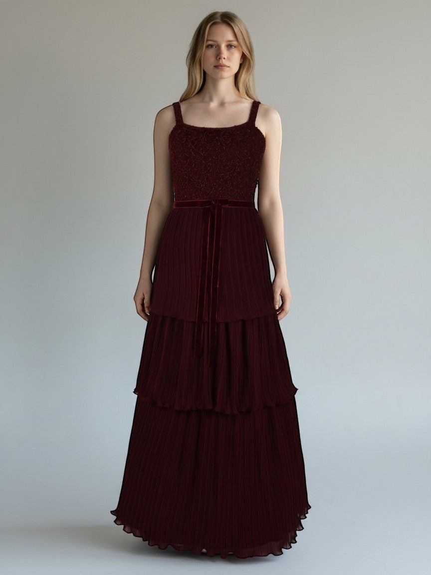 Ageless.ee deep burgundy tiered pleated maxi dress with embellished bodice, velvet waistband, and delicate straps. Model is wearing a formal evening gown.