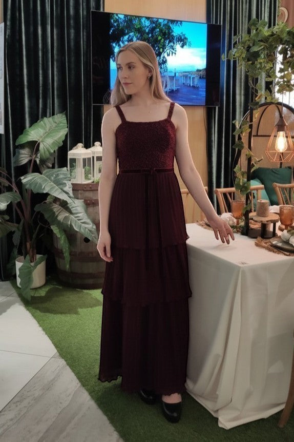 Ageless.ee deep burgundy tiered pleated maxi dress with embellished bodice, velvet waistband, and delicate straps. Model wears dress with black shoes.